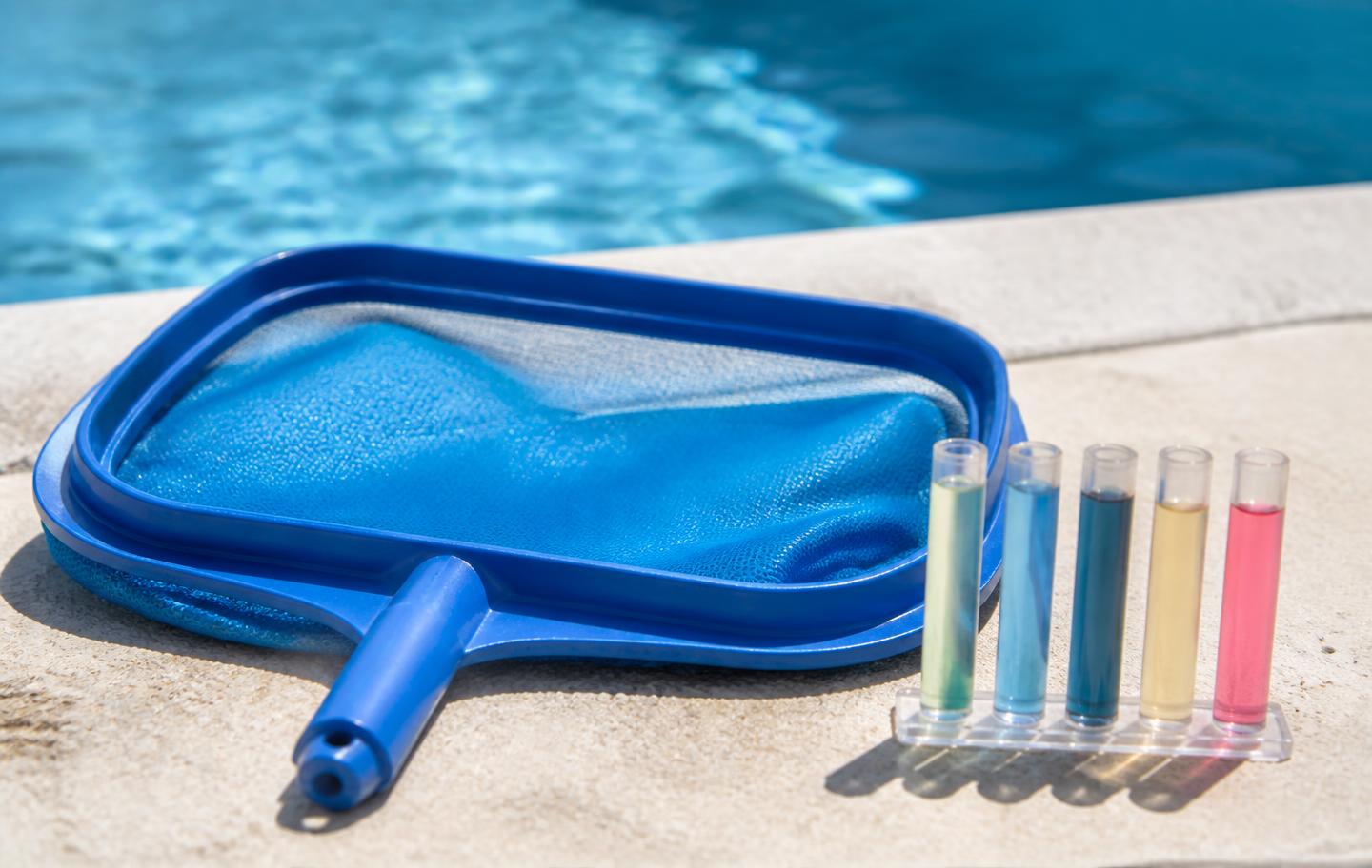 Pool skimmer net and water test vials on a sunlit pool deck