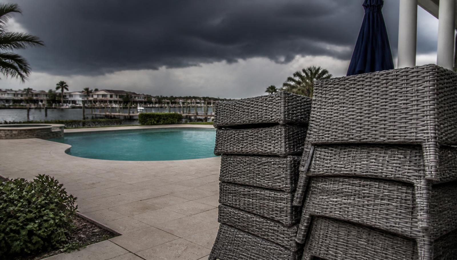 Patio furniture stacked beside a residential Florida pool under a dark storm sky
